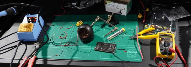 Soldering station setup — iron, helping hands, solder, side cutters and multimeter on a cutting mat
